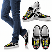 Black slip-on shoes with colorful designs and text, worn with blue jeans.
