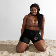Woman sitting on sand wearing a brown top and black shorts with a white logo.