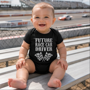 A smiling toddler wearing a "Future Race Car Driver" t-shirt, happily playing with colorful toy race cars on the floor of a brightly lit home garage.