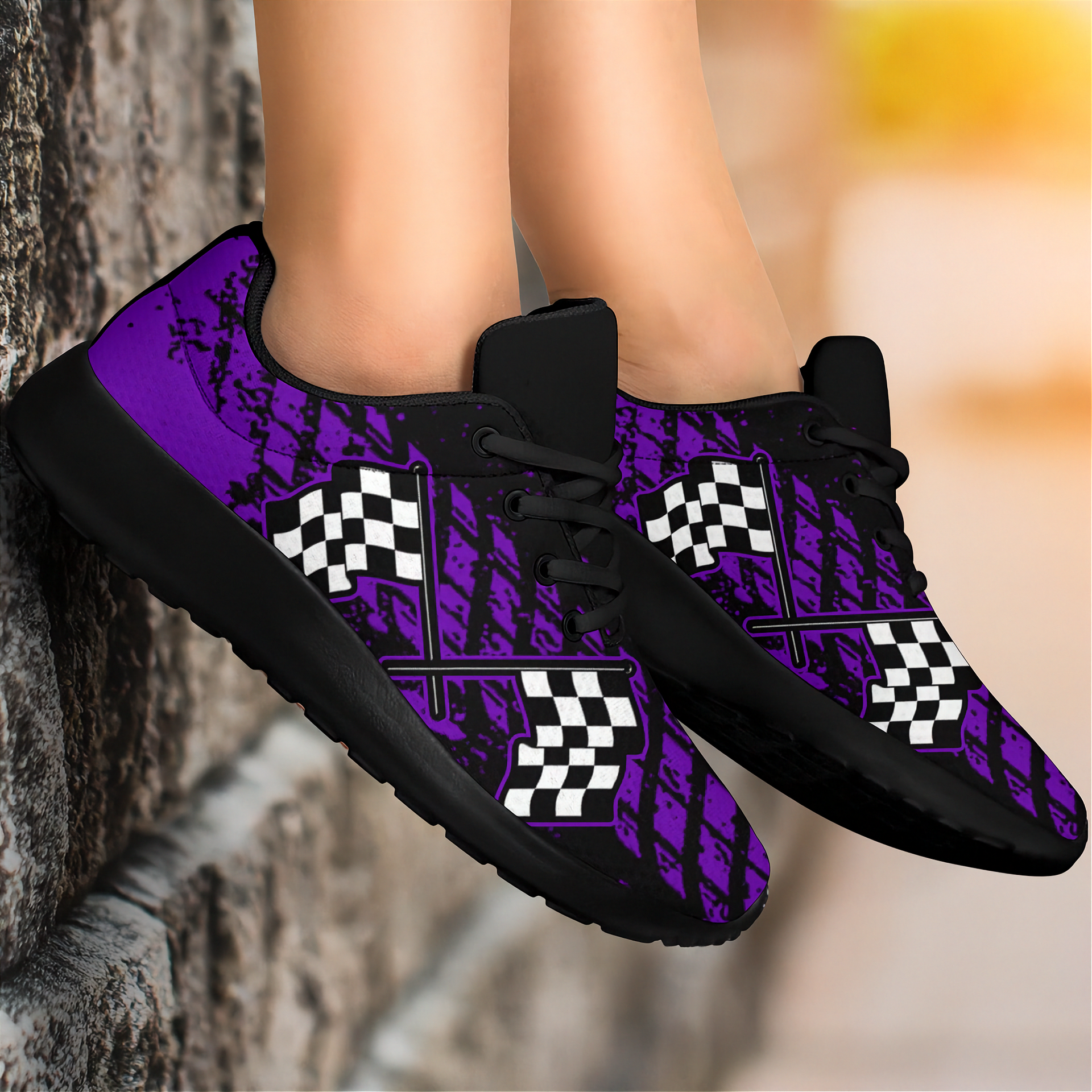 A pair of custom-designed dirt racing sneakers featuring a purple and black muddy tire track pattern with crossed checkered flags, shown from two different angles on a solid white background.