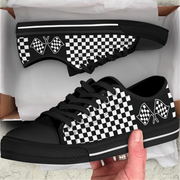 Black and white checkered sneakers with racing flag design held by a hand, displayed against a white background.