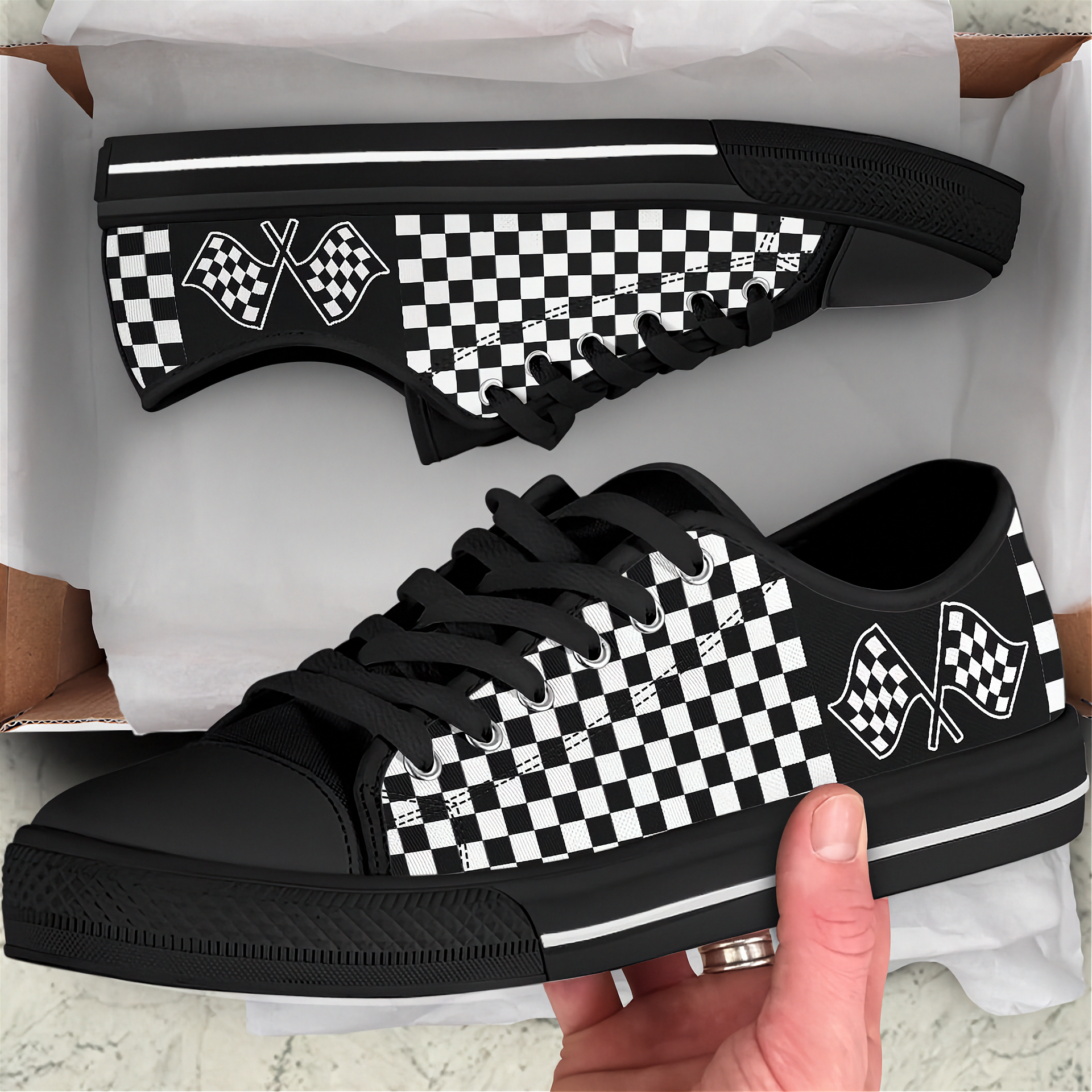 Black and white checkered sneakers with racing flag design held by a hand, displayed against a white background.