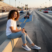 Woman sitting on a race track with cars in the background wearing a checkered flag low top shoes