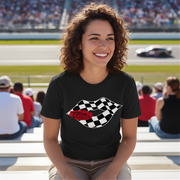 A trendy woman smiling while wearing a "Racing Checkered Lips" t-shirt and sunglasses, leaning against the side of a sleek sports car in a sunny outdoor parking lot.