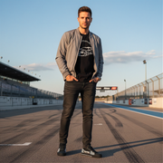 Man standing on a race track wearing a gray jacket and black jeans and racing low top shoes