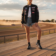 girl wearing a varsity jacket with patches on a wooden platform at a race track wearing a checkered pattern low top racing shoes.