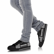 Black sneakers with checkered pattern worn with gray jeans on a white background