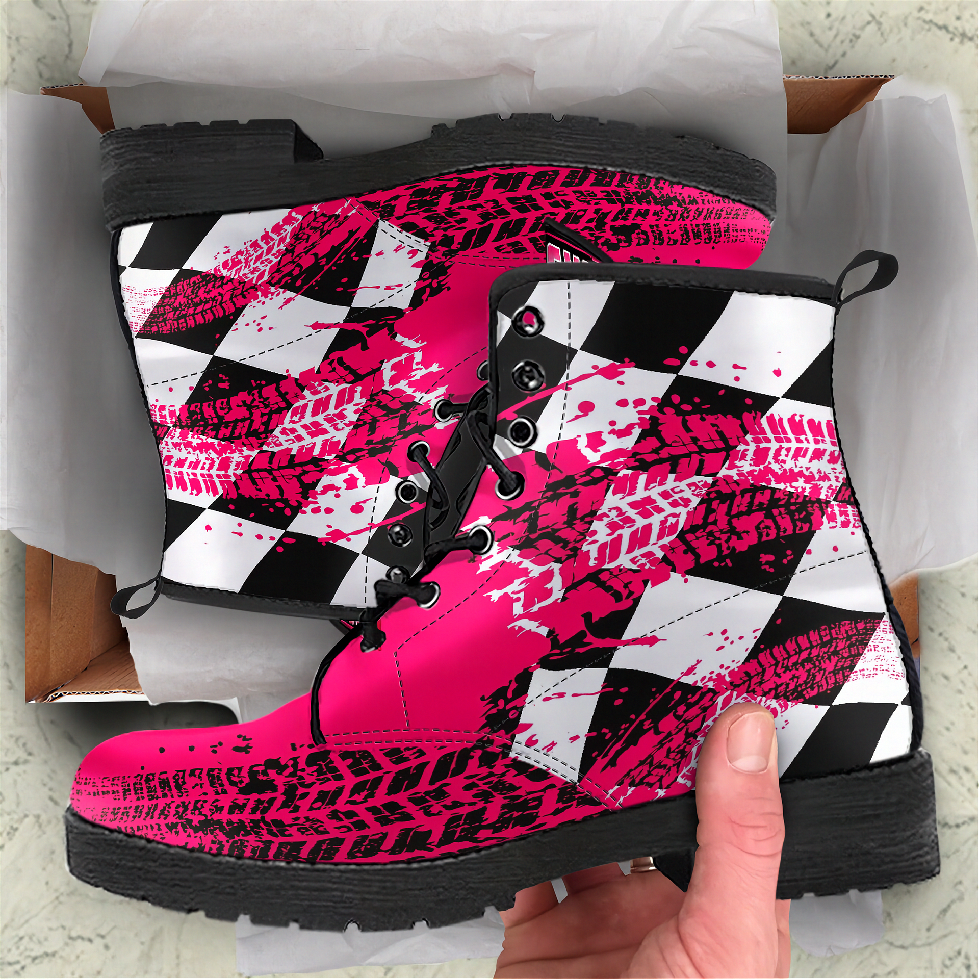 Pink, black, and white patterned boots held by a hand with a box in the background