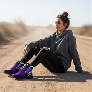 Woman sitting on a dirt road wearing a gray hoodie and black pants with purple checkered boots.