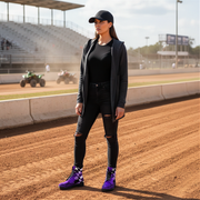 Woman standing on a dirt track wearing black outfit and purple racing flag boots