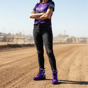 woman wearing a purple and black outfit with matching checkered boots on a dirt track.
