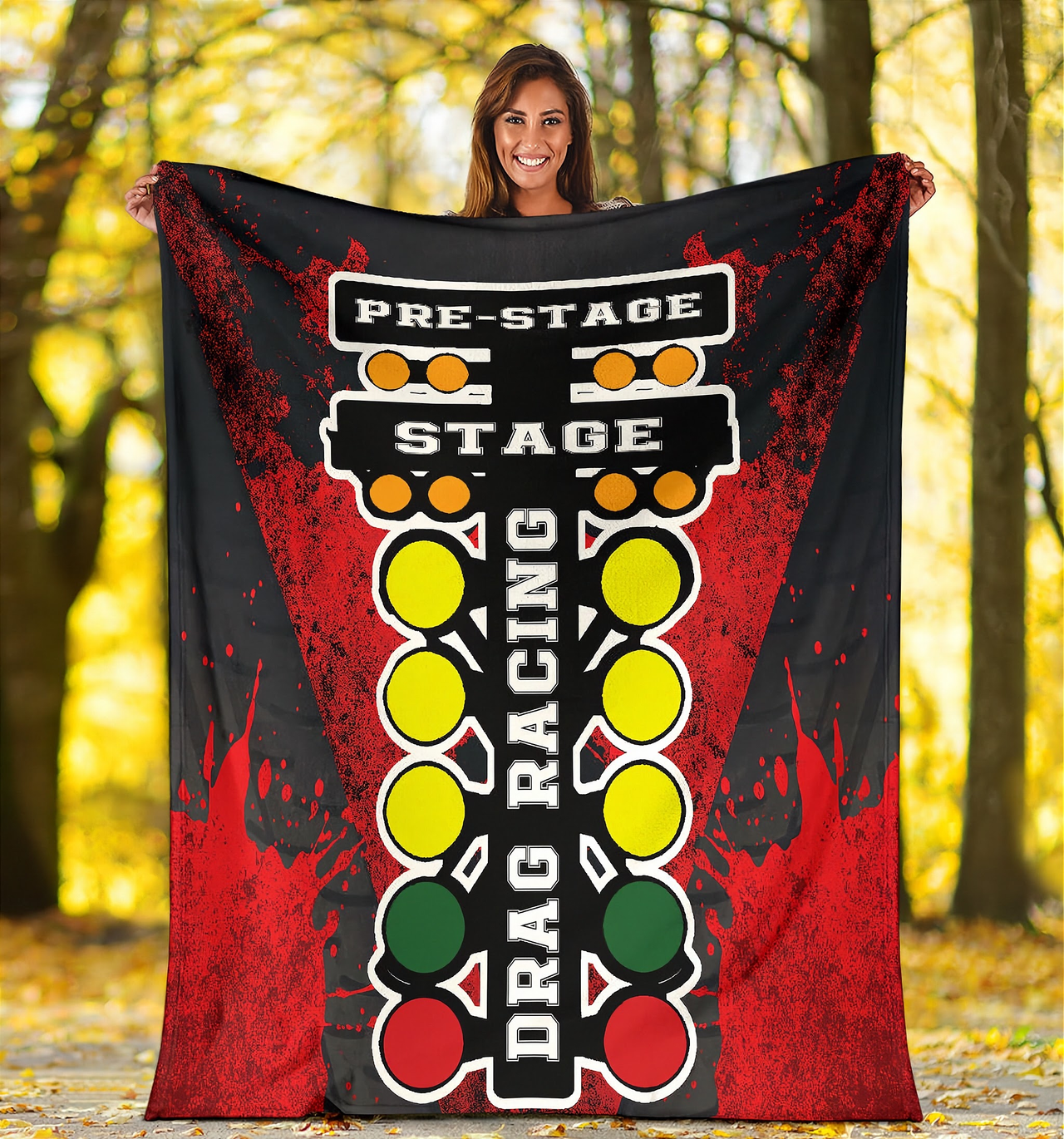 A vibrant red throw blanket with a high-definition graphic print of a launching dragster and a starting line Christmas tree, neatly folded on a neutral-colored couch.