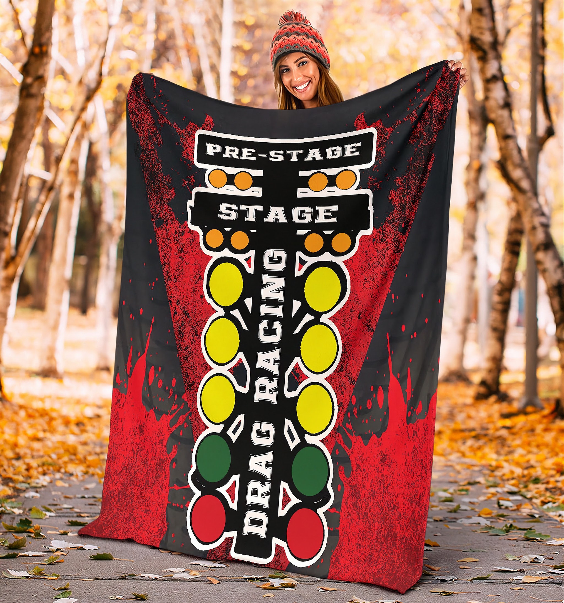 A vibrant red throw blanket with a high-definition graphic print of a launching dragster and a starting line Christmas tree, neatly folded on a neutral-colored couch.