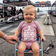 Child in a pink onesie with a racing theme at a drag racing event.