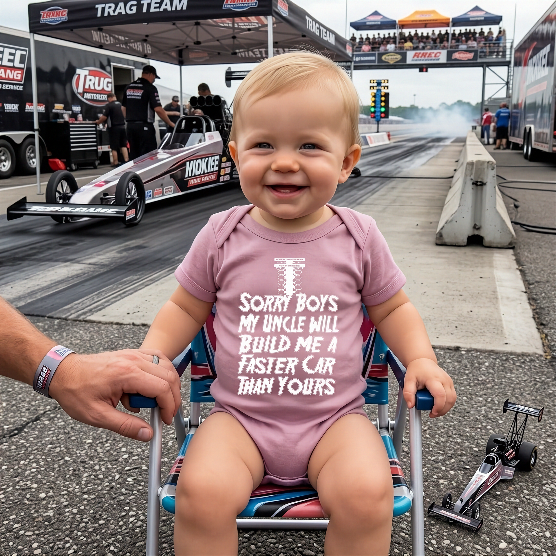 Child in a pink onesie with a racing theme at a drag racing event.