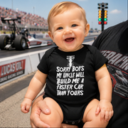 Baby wearing a black onesie with a humorous message, sitting on a person's lap at a race track.