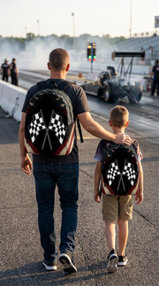 A young adult male wearing a patriotic USA checkered flag racing backpack, standing in the bustling fan zone of an American stock car race track with grandstands and colorful team haulers blurred in the background.