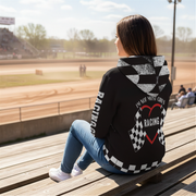 A stylish female race fan wearing the black "I'm Not Most Girls" sherpa jacket, with the hood up, standing under the bright LED lights of a racetrack grandstand, focusing on the textured lining and bold print.