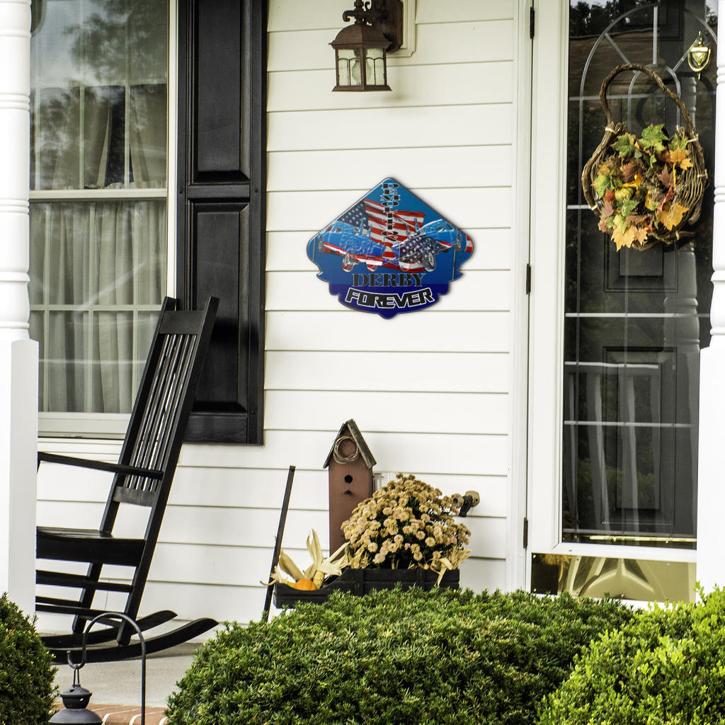 Demolition Derby Forever sign beside a front door, black rocking chair and seasonal plants.