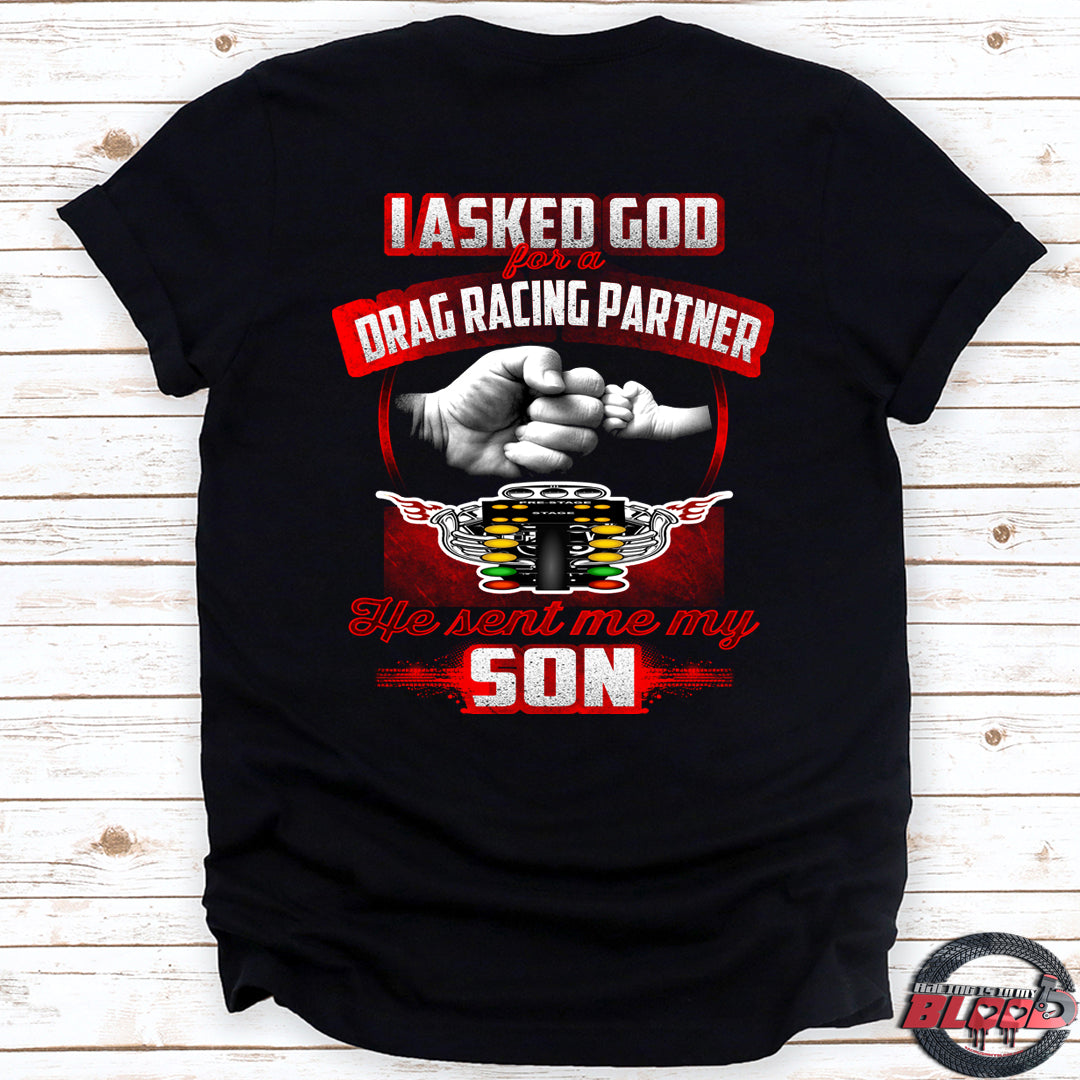 Heartfelt drag racing apparel featuring a fist-bump graphic and the text "I Asked God For A Drag Racing Partner He Sent Me My Son," available in t-shirts, tanks, and hoodies.
