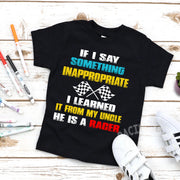 Black youth t-shirt with text 'If I say something inappropriate I learned it from my uncle he is a Rager' printed on it, presented on a wooden surface with markers and other crafting materials around it.