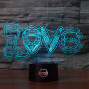 Love Motocross 3D LED Lamp showing a dirt bike rider jumping through a heart-shaped silhouette, glowing in a vibrant pink on a modern black base.