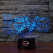 Love Motocross 3D LED Lamp showing a dirt bike rider jumping through a heart-shaped silhouette, glowing in a vibrant pink on a modern black base.