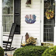 Patriotic Racing Forever sign beside a front door, black rocking chair and seasonal plants.