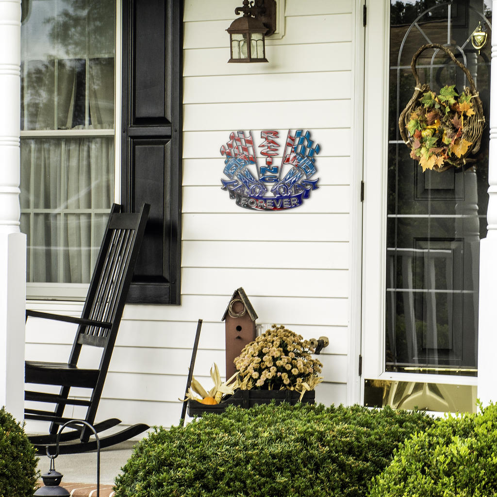 Patriotic Racing Forever sign beside a front door, black rocking chair and seasonal plants.