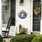 Patriotic sprint car metal sign beside a front door, black rocking chair and seasonal plants.