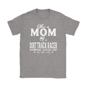 Premium black apparel mockup featuring a woman sitting on the wooden grandstand bleachers at a dirt track arena, wearing a soft custom t-shirt with a bold white graphic that reads "I'm a MOM of a DIRT TRACK RACER nothing scares me".