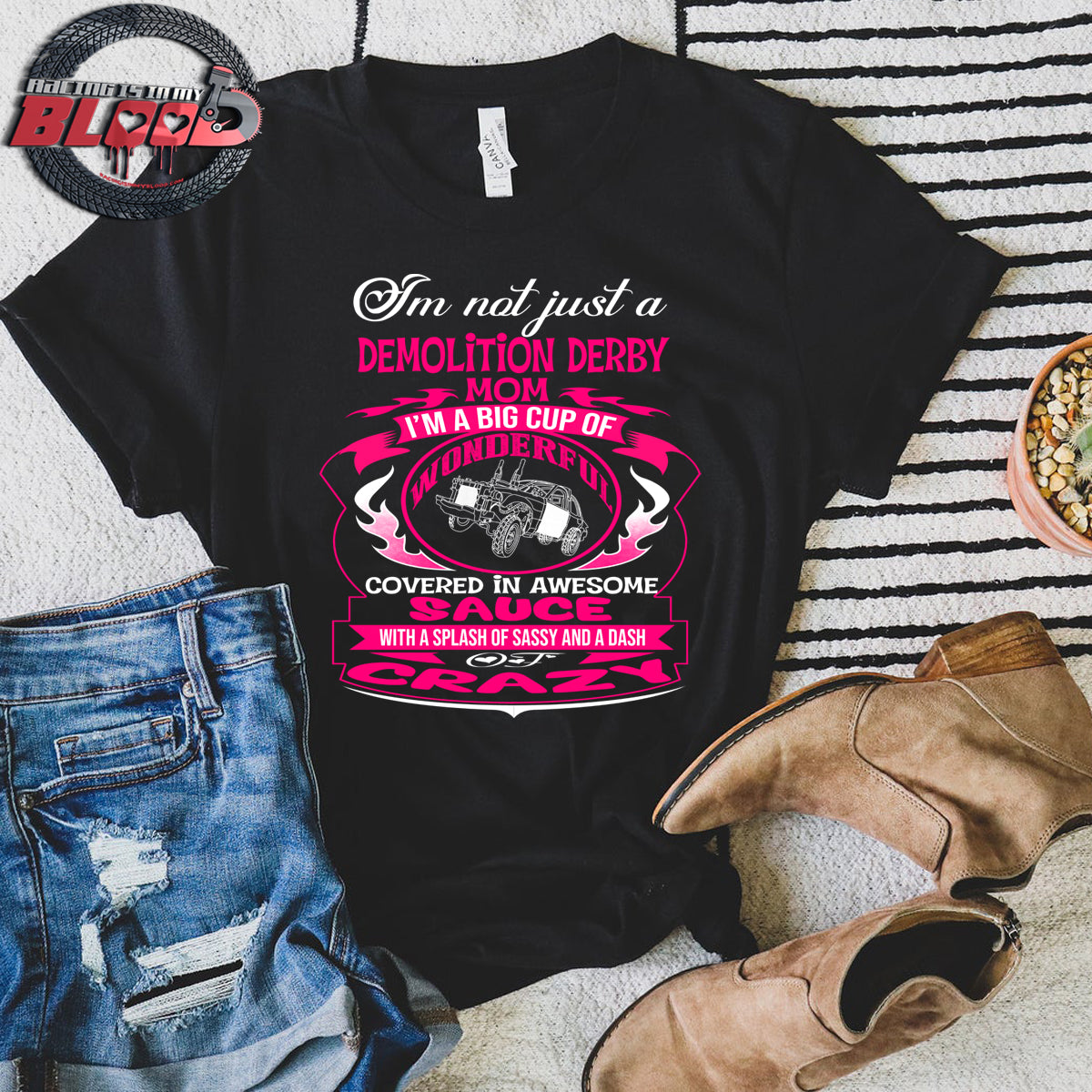 Premium women's black graphic t-shirt mockup featuring a vibrant pink and white custom design that reads "I'm not just a Demolition Derby Mom, I'm a big cup of wonderful covered in awesome sauce with a splash of sassy and a dash of crazy" with a derby car illustration.