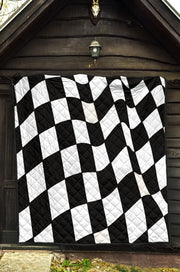 A black and white checkered quilted blanket is held up outdoors in a grassy field.