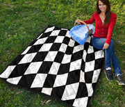 A woman sitting on a black and white checkered quilted blanket in a grassy field under a blue sky with clouds.