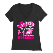 Woman sitting in the grandstands at a race track wearing a dark gray v-neck t-shirt with a pink and white graphic that reads "My Husband Is Faster Than Your Husband" alongside a race car and checkered flags.