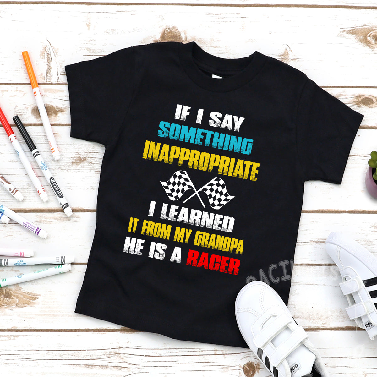 A collection of a youth t-shirt, baby bodysuit, and hoodie displaying the funny quote "If I Say Something Inappropriate I Learned It From My Grandpa He Is A Racer" in bold, playful typography with racing flag accents, set against a clean white background.