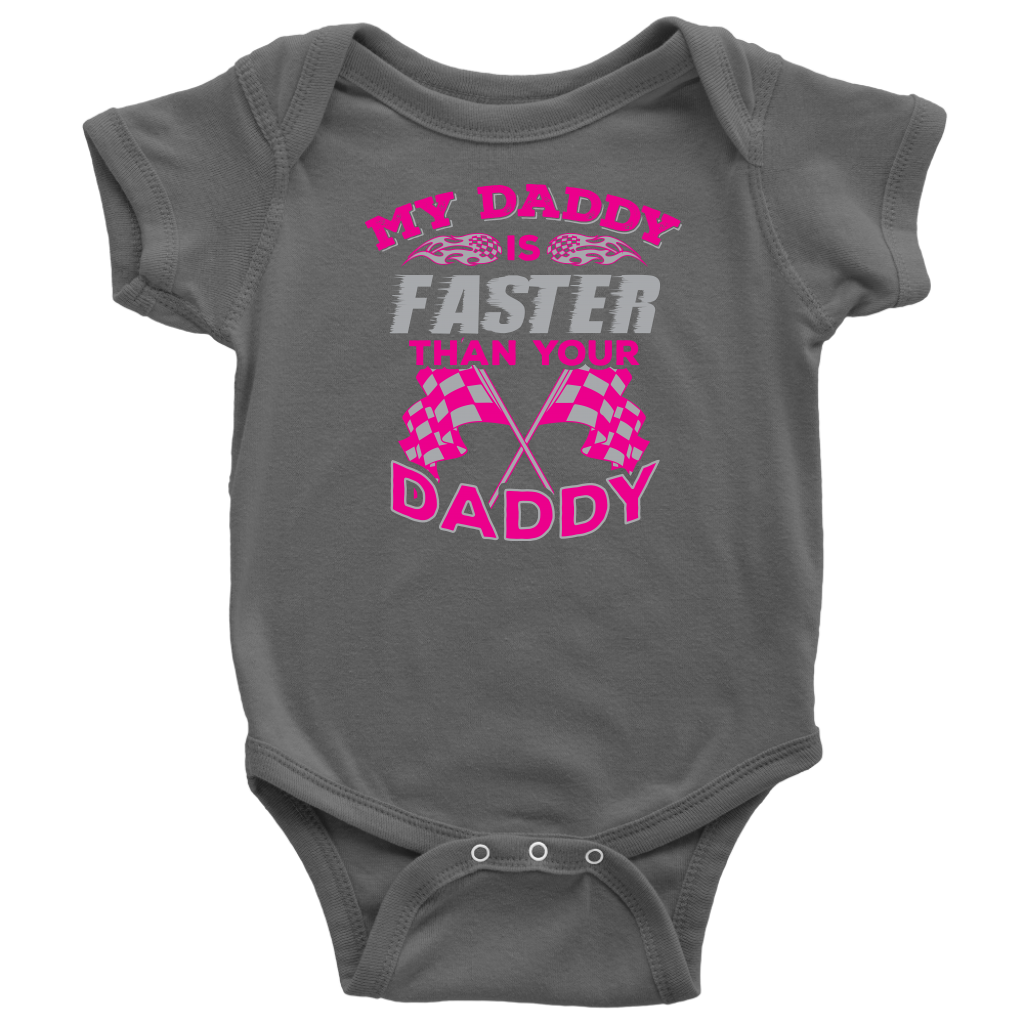 A proud, smiling racing dad in a fire suit holding his baby, who is wearing a cute "My Daddy Is Faster Than Your Daddy" bodysuit, standing confidently next to a colorful race car in the pit area.
