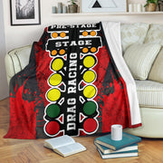 A vibrant red throw blanket with a high-definition graphic print of a launching dragster and a starting line Christmas tree, neatly folded on a neutral-colored couch.