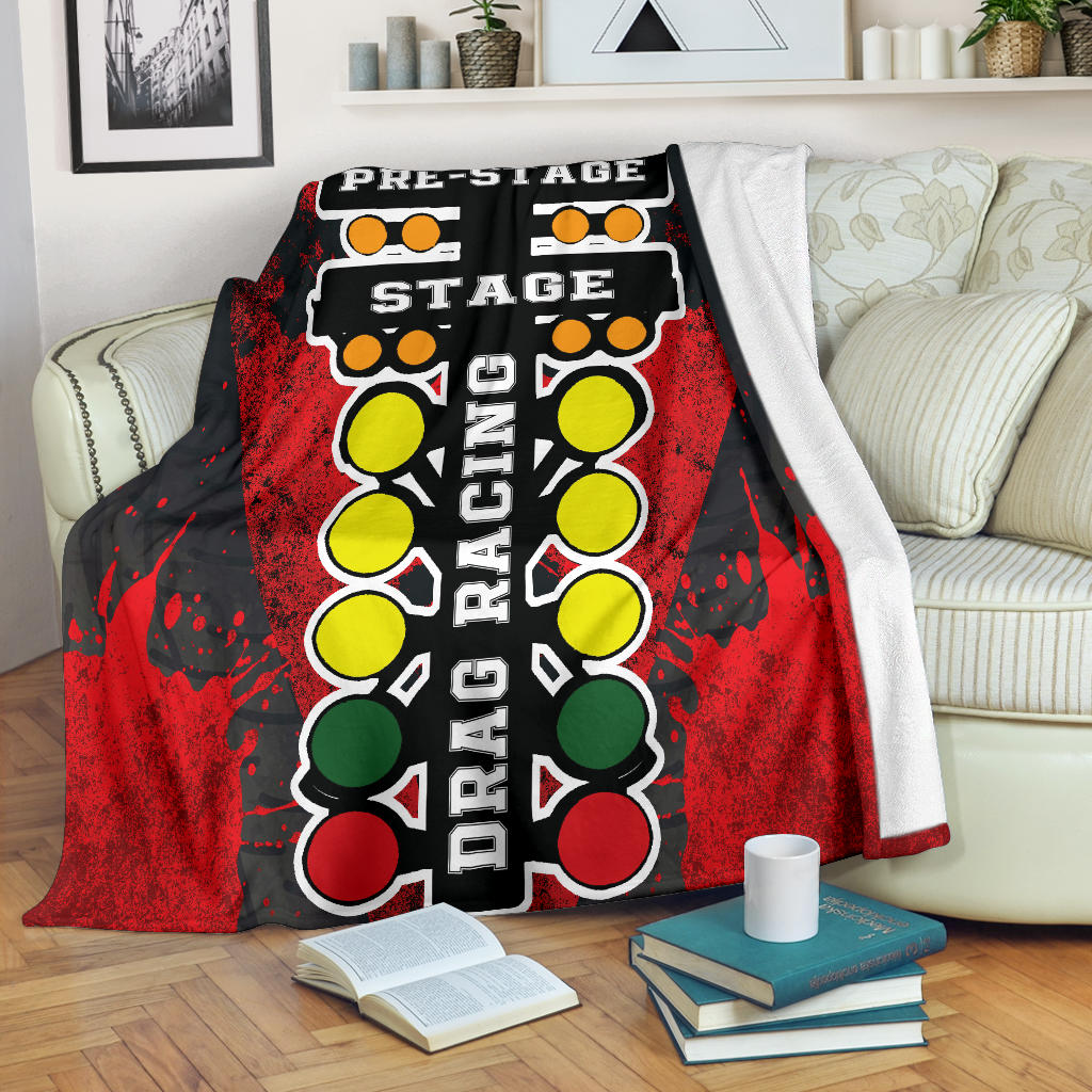 A vibrant red throw blanket with a high-definition graphic print of a launching dragster and a starting line Christmas tree, neatly folded on a neutral-colored couch.
