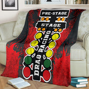 A vibrant red throw blanket with a high-definition graphic print of a launching dragster and a starting line Christmas tree, neatly folded on a neutral-colored couch.