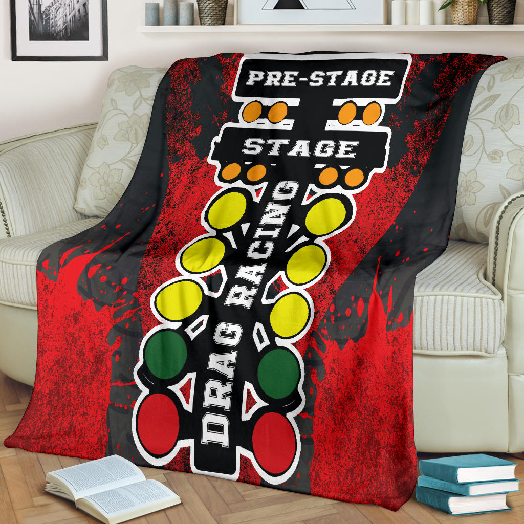 A vibrant red throw blanket with a high-definition graphic print of a launching dragster and a starting line Christmas tree, neatly folded on a neutral-colored couch.